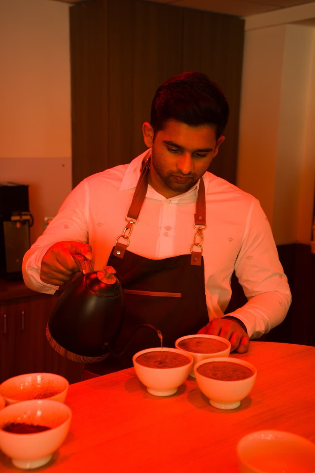 Pouring water over a row of cupping bowls at a cupping table